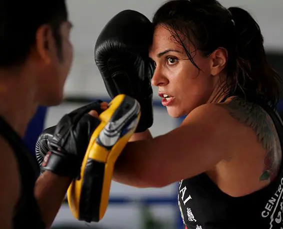 A woman is boxing in the gym with someone else.