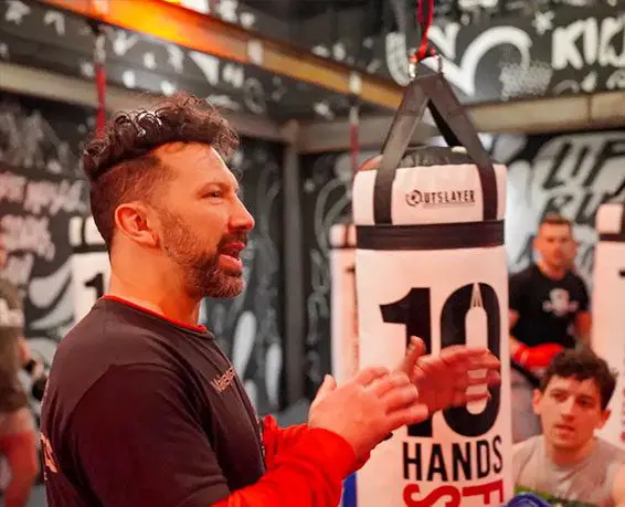 A man is speaking to people in front of a punching bag.